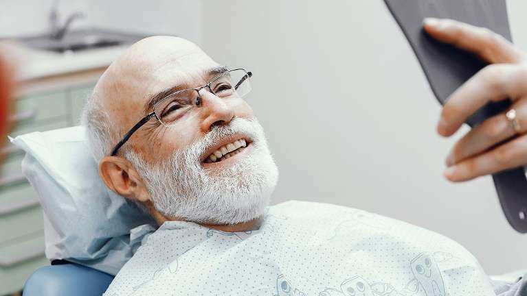 Smiling bearded man patient checking his teeth in a mirror in Florida